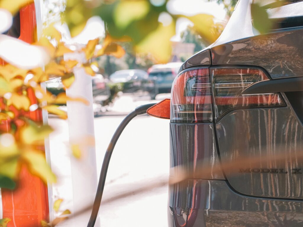 Close-up of an electric car connected to a charging station outdoors in sunlight.